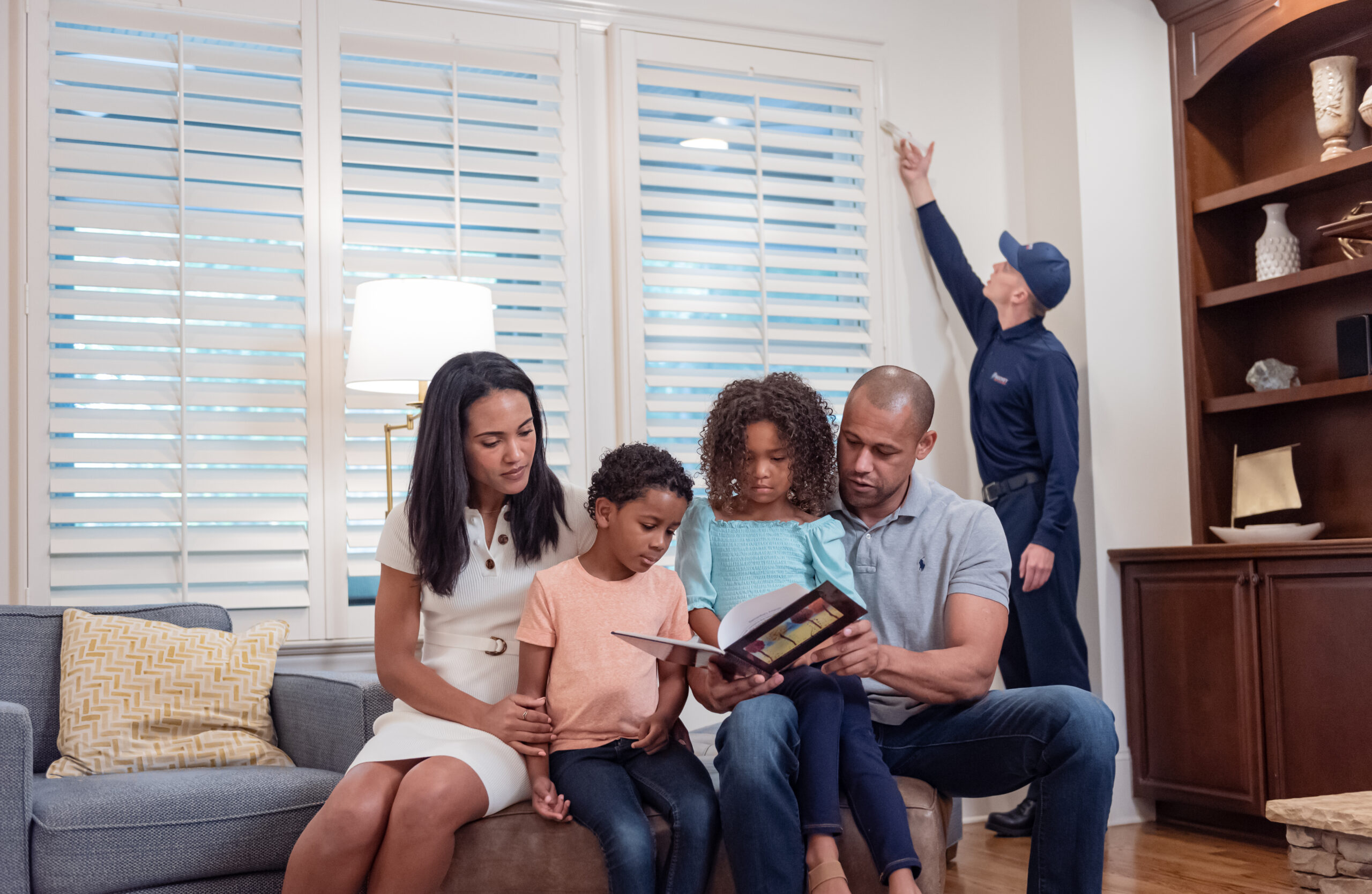 family sitting in a living room while a Rocket Pest Control exterminator treats a window for pests